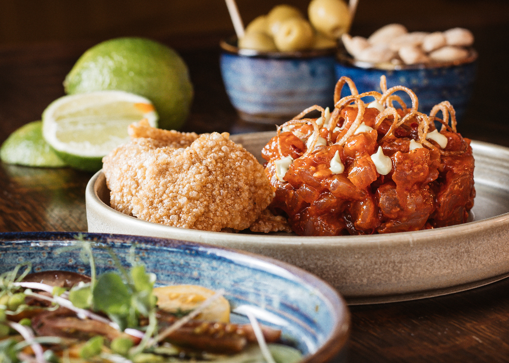 Bowl of Tuna Tartar with crab meat crackers. Lime wedges and bowls of nuts and olives in background